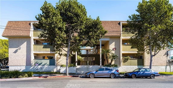 Front view of a multi-story residential building with balconies and a central archway entrance, surrounded by trees.