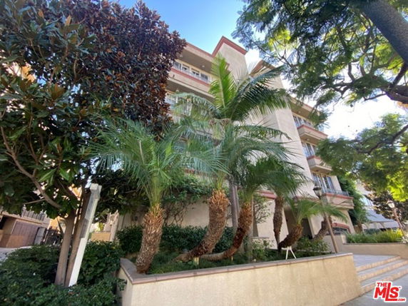 Front view of a multi-story building with balconies and surrounding trees.
