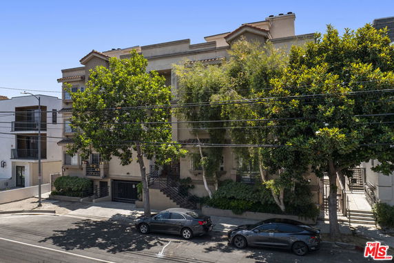 Front view of a multi-story residential building with trees and parked cars in front.