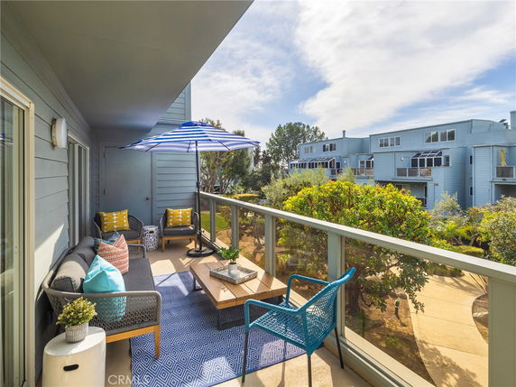 Balcony view showing a seating area with a table and umbrella, overlooking neighboring buildings and greenery.