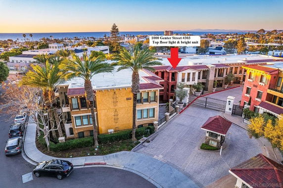 Aerial view of a residential complex near the ocean with palm trees and a gated entrance.