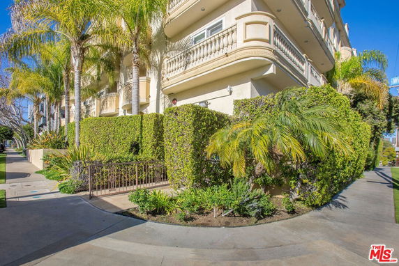 Corner view of a multi-story building with balconies and palm trees.