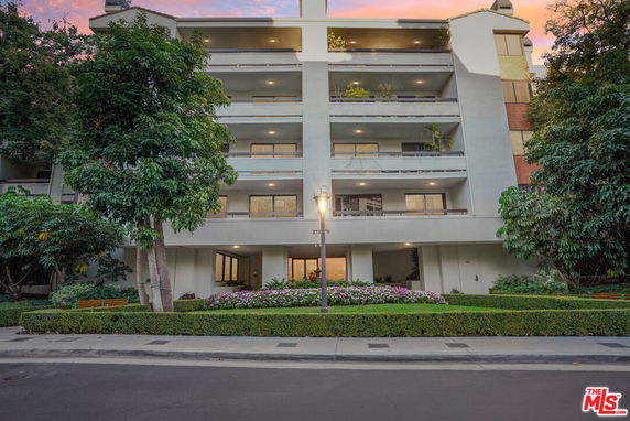 Front view of a multi-story residential building with balconies and surrounding greenery.