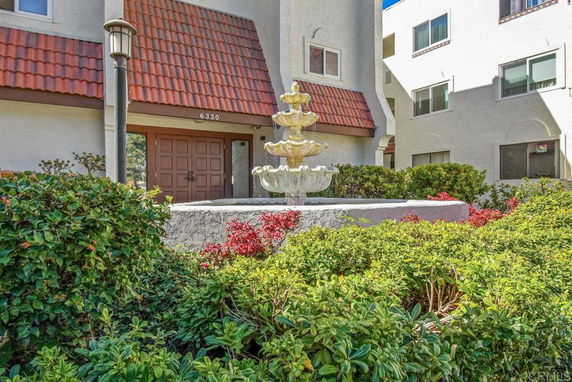 Front view of a multi-story building with a decorative fountain and gardens.