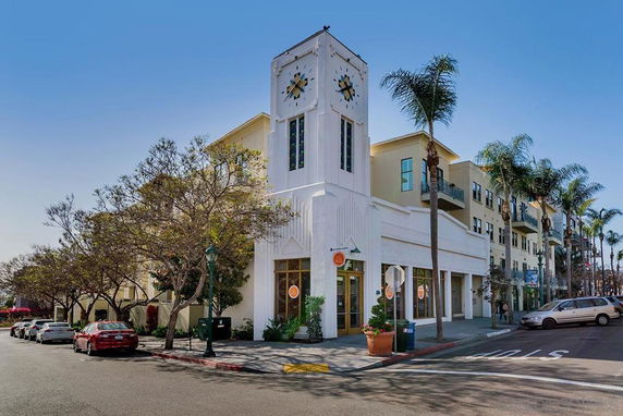 Front view of a multi-story building with a clock tower and palm trees.