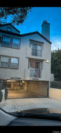 Front view of a multi-story building with balconies and a gated entrance to an underground parking area.