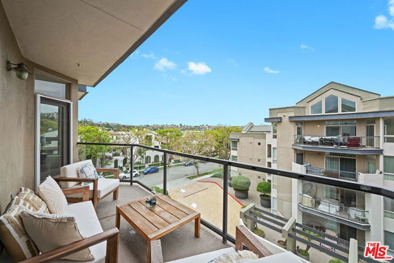 Panoramic view from a balcony overlooking residential buildings and a tree-lined street.