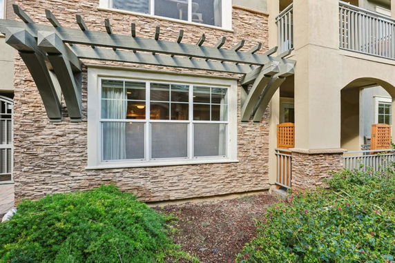 Front view of a building with stone facade and wooden trellis above a large window.