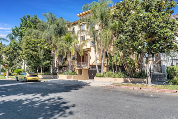 Front view of a multi-story residential building with palm trees and a yellow car parked in front.