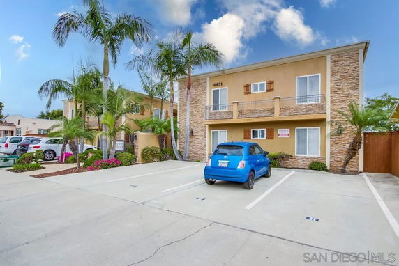 Outdoor parking area in front of a two-story building with palm trees.