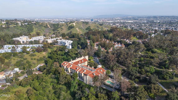 Aerial view of a residential area with multiple buildings surrounded by greenery and hills.