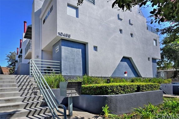 Front view of a modern multi-story building with a staircase and greenery.