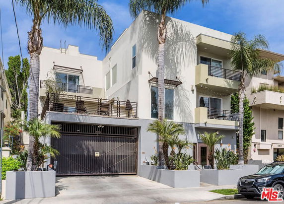 Front view of a modern multi-story building with balconies and palm trees.