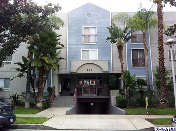Front view of a multi-story residential building with a central entrance and surrounding vegetation.