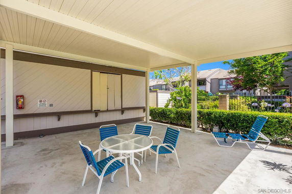 Covered outdoor seating area with chairs and a table, surrounded by greenery.