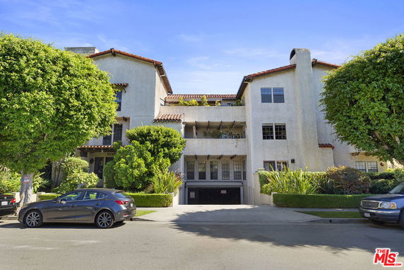 Front view of a multi-story apartment building with trees and parked cars.