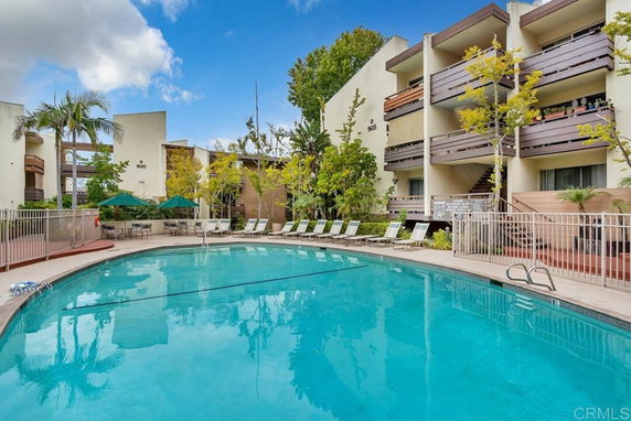 Outdoor swimming pool area surrounded by a multi-story residential building with balconies and trees.