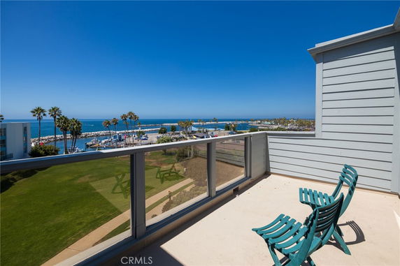 View of the ocean and marina from a rooftop area with chairs.