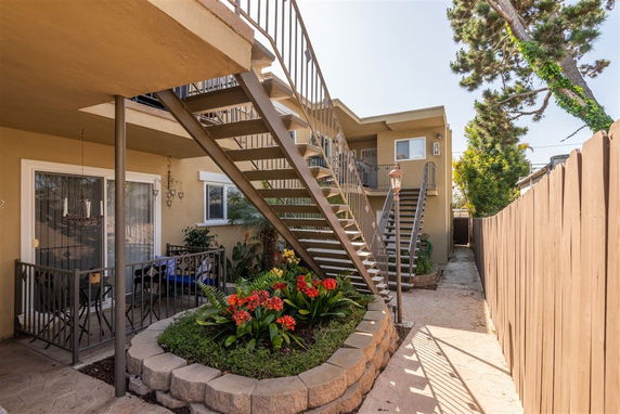 Front view of a two-story building with an exterior staircase and a small garden at the ground level.