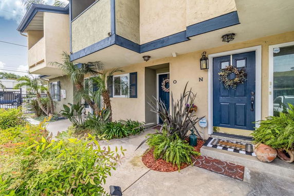 Front view of a two-story house with plants and a blue door.