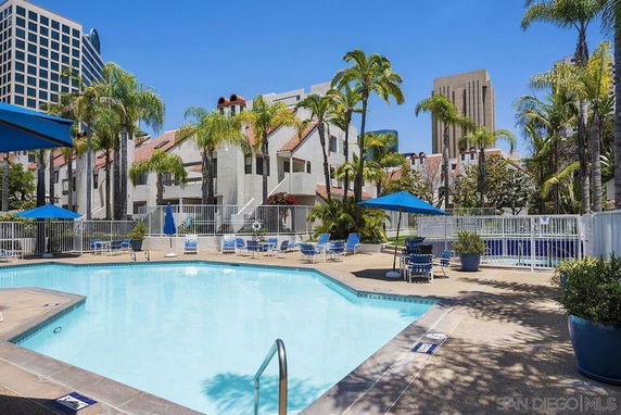 Outdoor swimming pool area with surrounding buildings and palm trees.