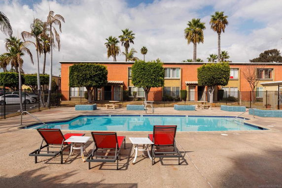 Swimming pool area in front of a two-story building with palm trees.