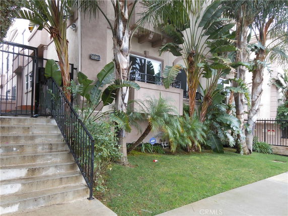 Front view of a multi-story building with stairs and tropical plants.