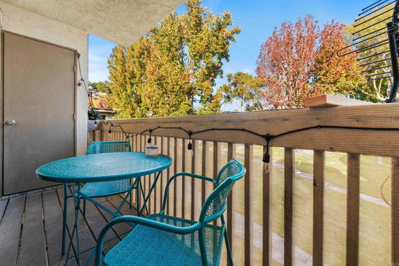 Small balcony with turquoise table and chairs overlooking trees.