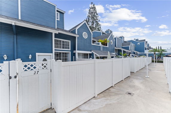 Front view of a row of multi-story blue townhouses with white fencing.