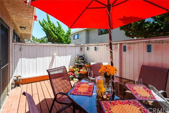 Outdoor patio area with a red umbrella, glass table, and chairs surrounded by wooden fencing.