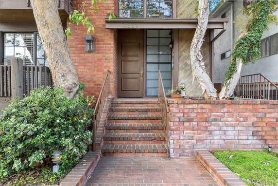 Front view of a brick house entrance with stairs and trees.
