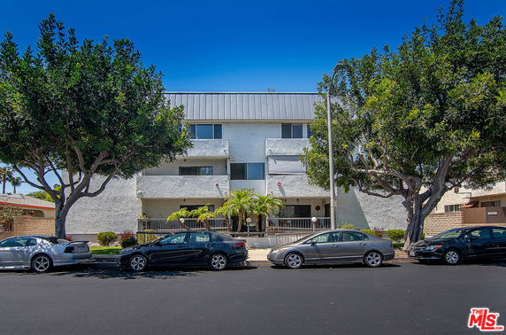 Front view of a multi-story building with balconies and parked cars.