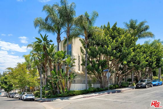 Front view of a multi-story building surrounded by trees and parked cars.