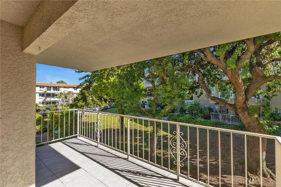 Balcony view of a garden area with trees and nearby buildings.