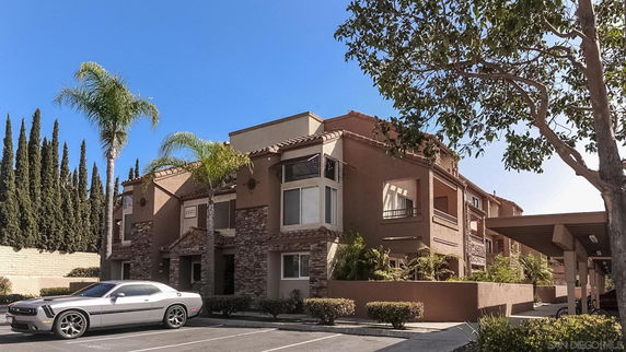 Front view of a multi-story residential building with parking area and landscaping.