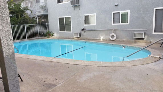 Outdoor swimming pool adjacent to a building with windows and a safety railing.
