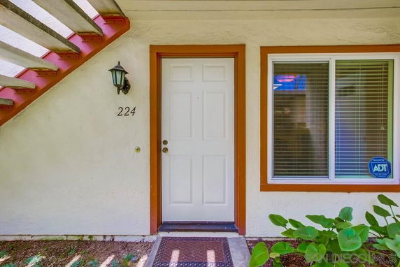 Front view of an apartment entry with a white door, window, and staircase above.