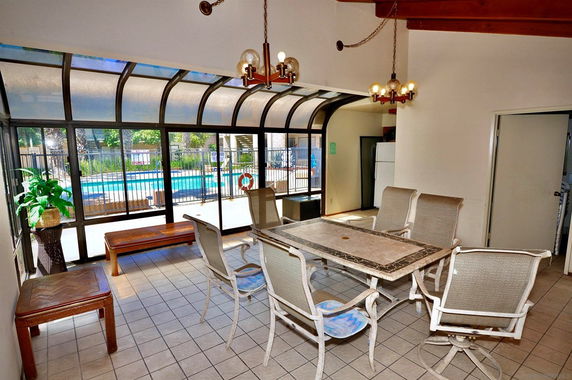 Indoor recreation area with a dining table and chairs, large windows overlooking a swimming pool.