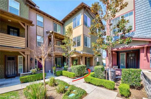 Front view of a multi-story townhouse with balconies and decorative shrubs.