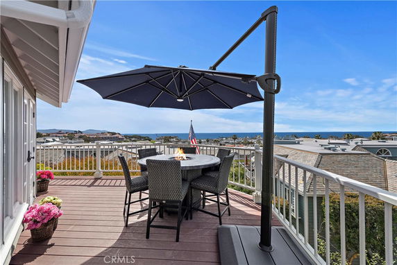 Terrace with seating and umbrella offering a view of rooftops and the ocean.