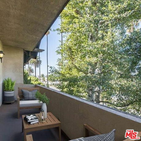 Outdoor balcony area with seating and view of trees and palm trees.