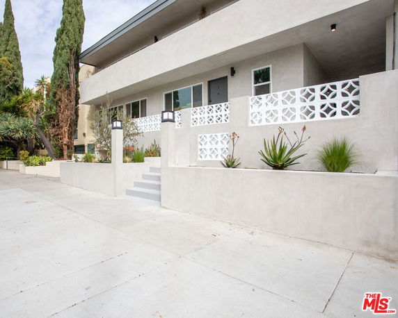 Front view of a modern building with geometric railing and landscaped planters.