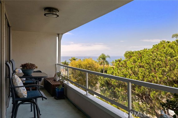 Balcony with chairs and railing overlooking a scenic landscape with trees and distant ocean.