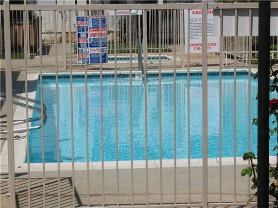 Outdoor swimming pool with safety fence and warning signs.
