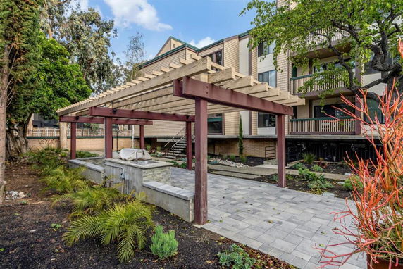 Front view of a multi-story residential building with balconies and a wooden pergola.