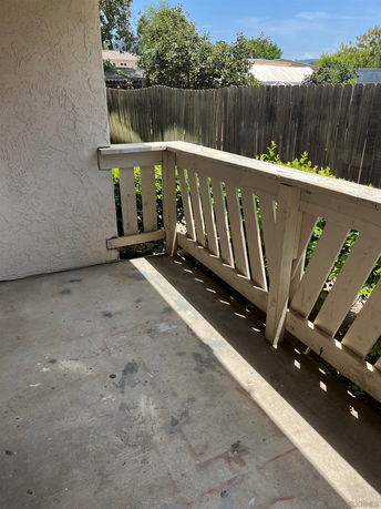 Outdoor patio area with wooden railing and a view of a fence and trees.