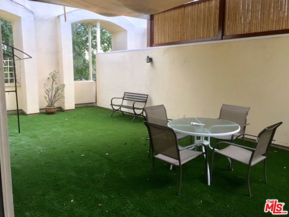 Outdoor area with artificial grass, a round table, and chairs under a covered section.