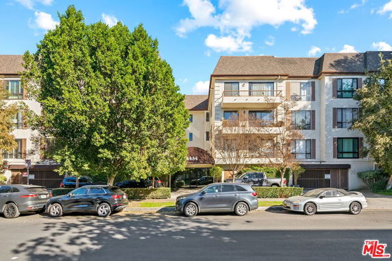 Front view of a multi-story residential building with balconies and trees in front.