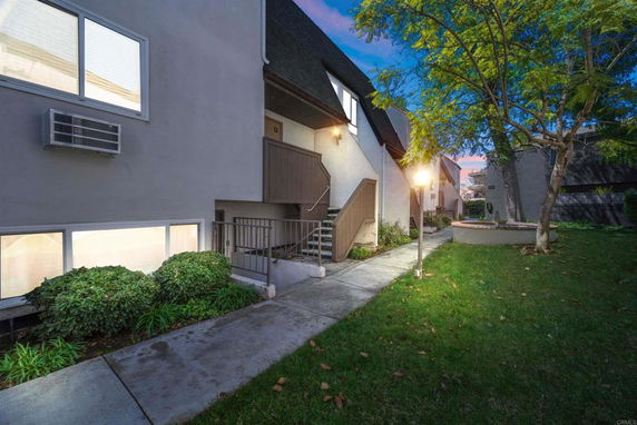 Front view of a multi-story building with exterior staircase and small garden.
