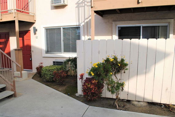 Front view of an apartment unit with a red door and a small outdoor area.